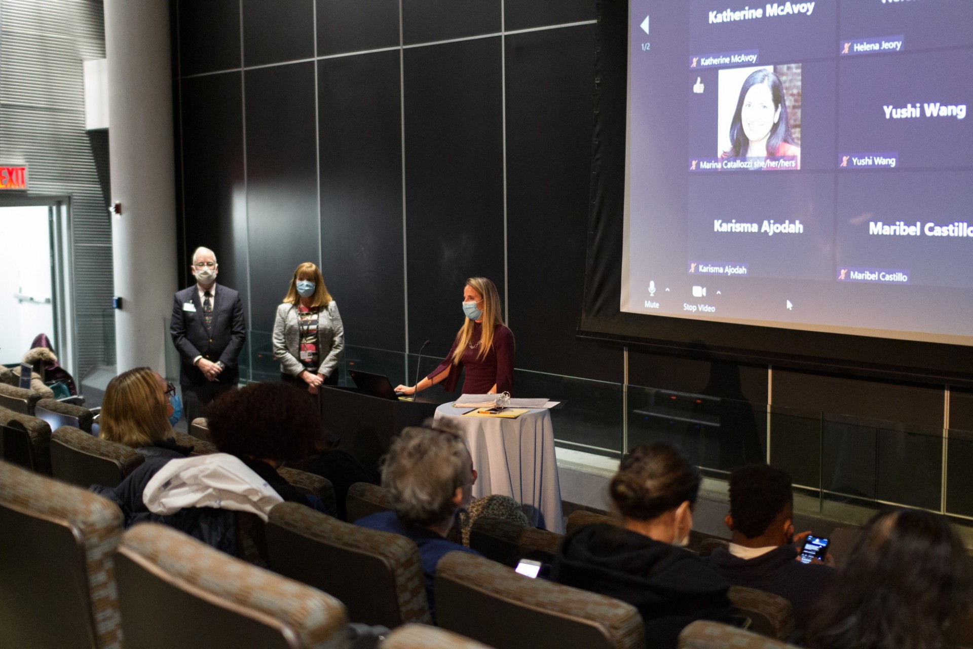 Dr. Melanie Berntiz (SVP, Columbia Health) welcomes AAAHC surveyors at the closing session Three individuals standing in front of an audience sitting in a cinema