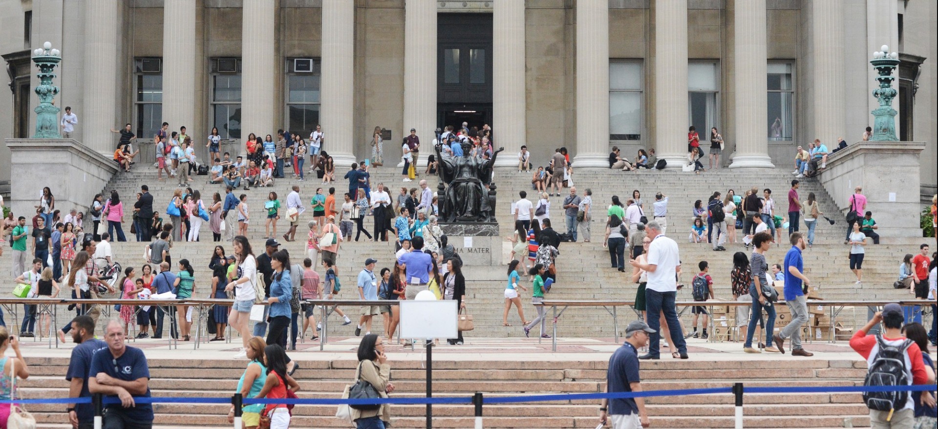 Crowd of people standing or sitting in front of Low Library steps and walking along College Walk