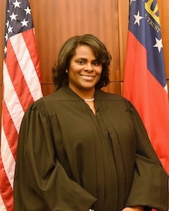 Judge Monique Walker in judicial robes sitting between two flags 