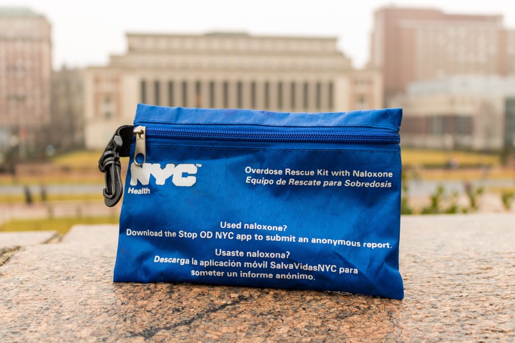 Blue naloxone kit sitting on ledge with campus buildings in background