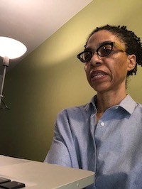 Dr. Addette Williams speaking with a student. Woman wearing glasses speaking while sitting in front of a desk