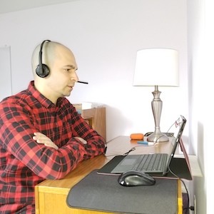 Man wearing headset speaking while looking at a laptop.