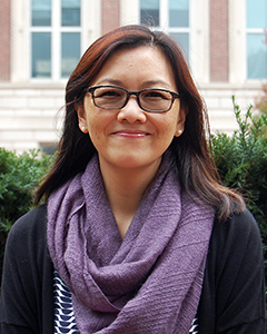 Individual with long hair and glasses smiling into camera