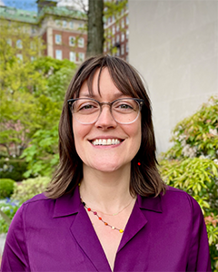 Individual with glasses and long hair smiling into camera