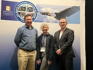 Three individuals standing underneath a U.S. Health Promoting Campuses Network banner