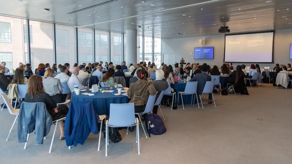 Conference room with a group of people seated around tables watching a presentation